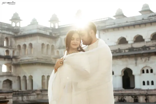 The couple wrapped in a dupatta, backlit at a fort